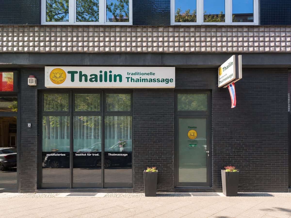 Außenansicht von Thailin Thaimassage: dunkle Klinkerfassade mit grünem Schriftzug „Thailin – traditionelle Thaimassage“ über der Fensterfront.